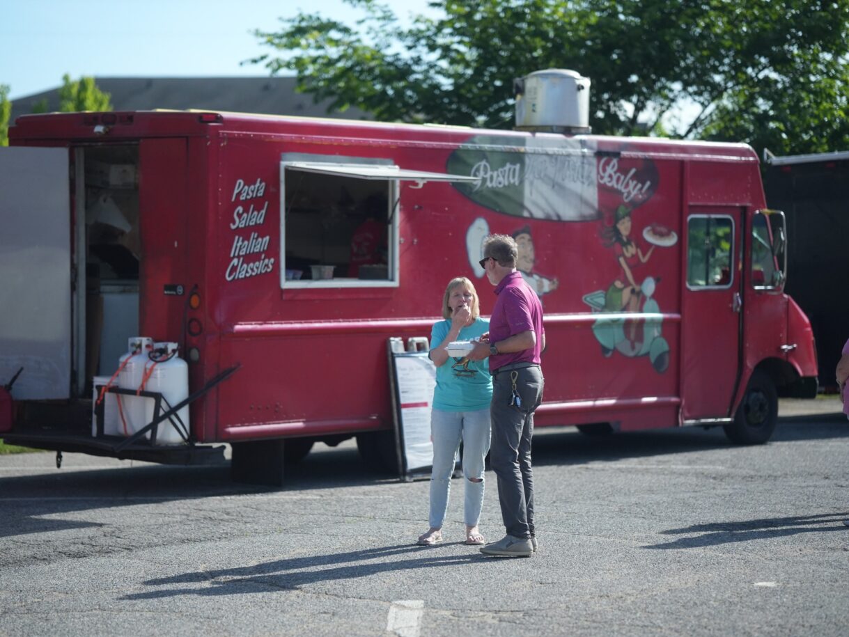A red food truck named "Pasta Baby!" with two people standing in front of it.