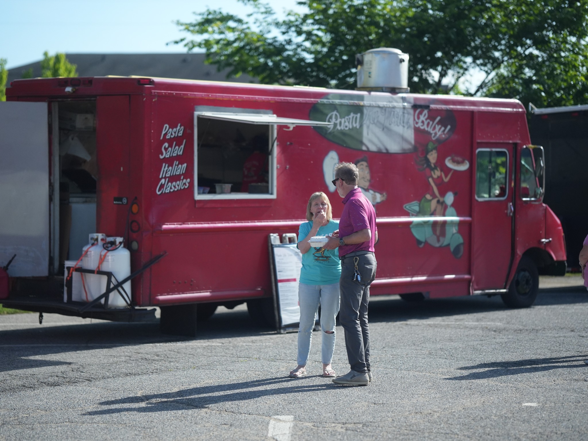 A red food truck named "Pasta Baby!" with two people standing in front of it.