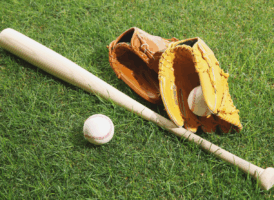 A baseball bat, two baseball gloves, and a baseball resting on green grass.