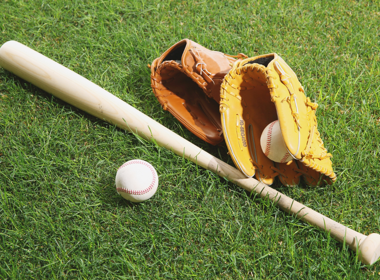 A baseball bat, two baseball gloves, and a baseball resting on green grass.