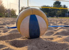 A yellow, white, and blue volleyball resting on sand on a beach volleyball court.