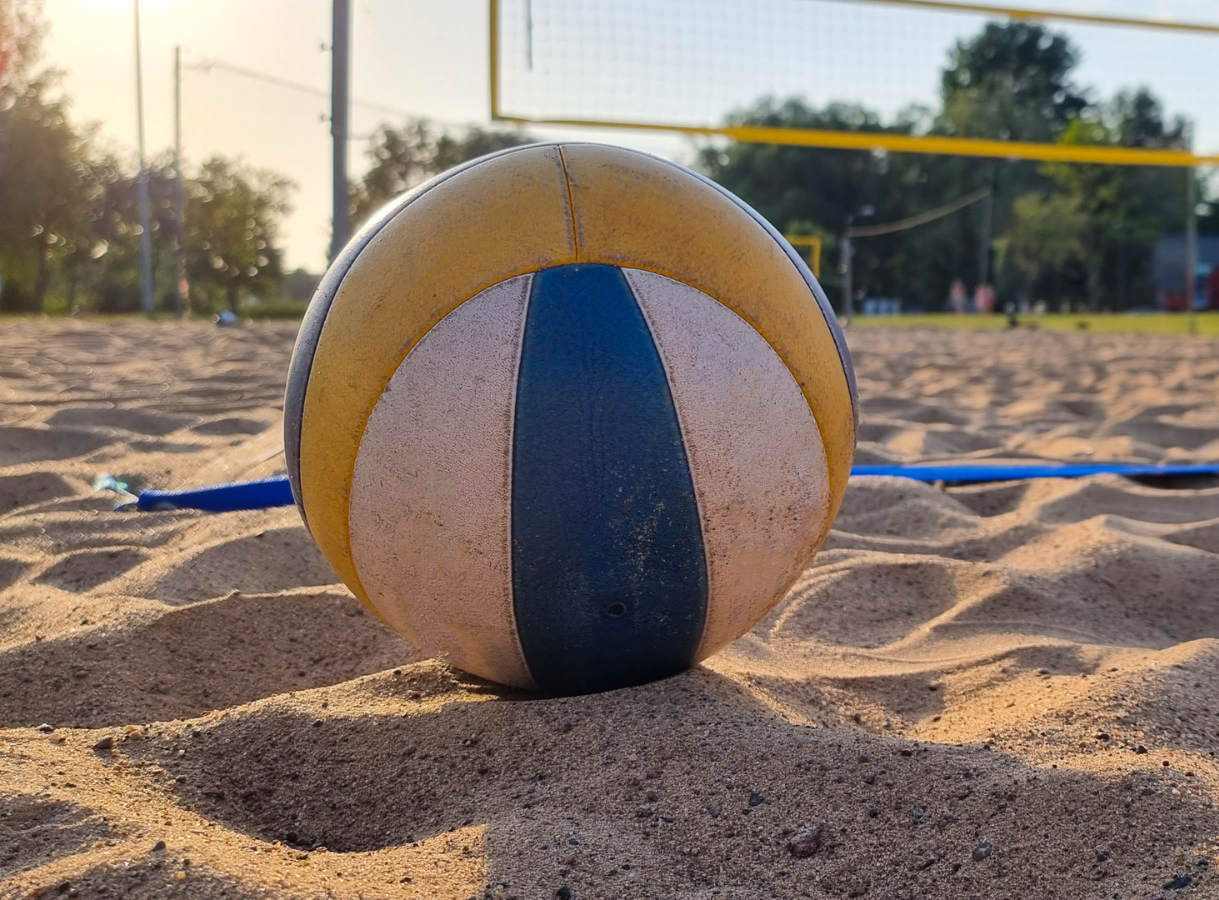 A yellow, white, and blue volleyball resting on sand on a beach volleyball court.