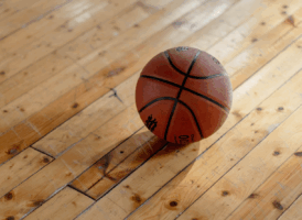 A brown basketball with black grooves sits on a light-colored wooden floor.